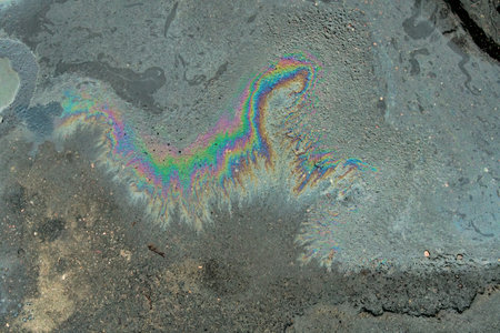 Rainbow-colored oil floating on water after rain on asphalt. Gasoline stains. Colored texture, natural background.の写真素材