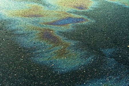 Textured stain of fuel or oil on wet asphalt on a rainy day.