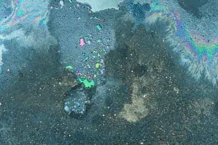 Rainbow-colored oil floating on water after rain on asphalt. Gasoline stains. Colored texture, natural background.の写真素材