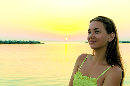 Close-up portrait of a young woman in a yellow dress at sunrise against the background of the sea. Woman walks on the seashoreの写真素材
