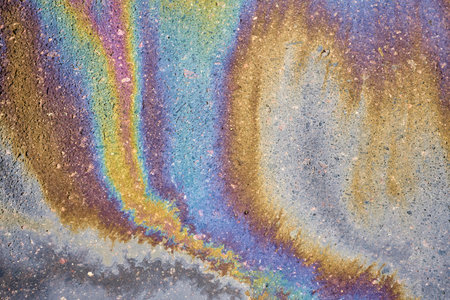 Close-up of an iridescent oil or gasoline spill on a wet asphalt, viewed from above. Bold multicolored spots on the asphalt. Concept of environmental problemsの写真素材