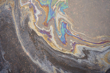 Rainbow-colored oil floating on water after rain on asphalt. Gasoline stains. Colored texture, natural background.の写真素材