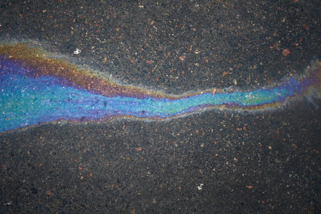 Multi-colored poisonous spots of spilled gasoline on wet pavement during rain. Rain blurred the car oil from a malfunctioning car in a parking lotの写真素材