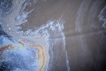 Close-up of an iridescent oil or gasoline spill on a wet asphalt, viewed from above. Bold multicolored spots on the asphalt. Concept of environmental problemsの写真素材