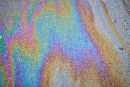 Multi-colored poisonous spots of spilled gasoline on wet pavement during rain. Rain blurred the car oil from a malfunctioning car in a parking lotの写真素材