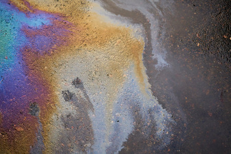 Rain washed away car oil or fuel flowing from a faulty car in a parking lotの写真素材