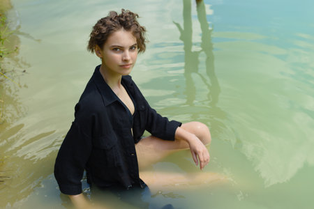 Young woman in a dark dress sits in the water.の写真素材