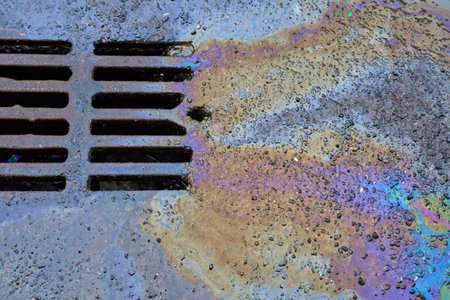 Close-up of an oil or gasoline stain against the backdrop of an asphalt road flowing into a storm drain. Environmental problems of water pollution.の写真素材