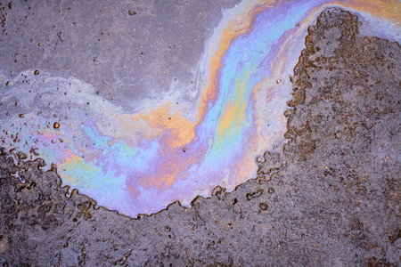 Fuel or oil spills on an asphalt road after melted snow as a texture or backgroundの写真素材