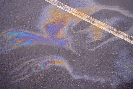 Fuel or oil spills on an asphalt road after melted snow as a texture or background. Oil spill on wet asphalt, parking lot with dividing line.の写真素材