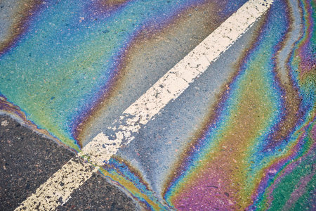Oil, gasoline, or fuel leakage on wet pavement in a parking lot marked with a dividing line