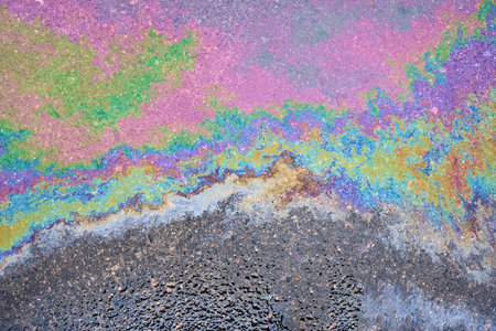 Captivating close-up of the opalescent sheen of a petrochemical spill on saturated asphaltの写真素材