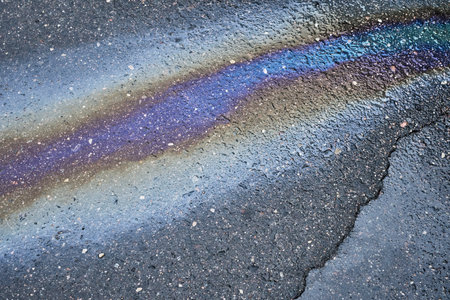 Oil spill dispersed across an asphalt road, generating a captivating abstract backdropの写真素材