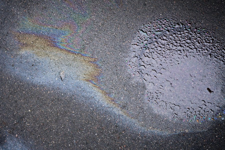 Rainbow gasoline spill creating colorful pollution on wet asphalt road.の写真素材