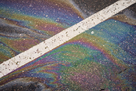 Vibrant oil or gasoline spill producing a rainbow-like sheen on a dark asphalt road, accented by a white traffic lineの写真素材