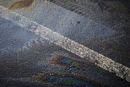 Multicolored oil spill generating a rainbow sheen on the dark pavement, complemented by a white traffic lineの写真素材