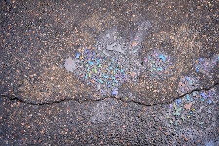 Colorful gasoline or oil spill creating a rainbow effect on cracked asphalt road surfaceの写真素材