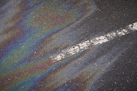 Colorful gasoline slick creating a shimmering rainbow effect on the dark asphalt, alongside a white road markingの写真素材