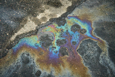 Gasoline or oil spill creates rainbow sheen on cracked asphalt surfaceの写真素材