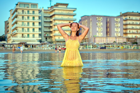Young woman standing in the sea in front of hotels, enjoying summer holidaysの写真素材