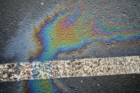 Colorful oil spill creating a striking pattern on asphalt near a parking lot.の写真素材
