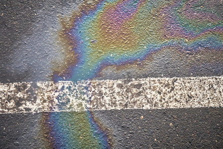 Damp asphalt in a parking area, displaying a fuel spill from a car, bordered with a white line.の写真素材