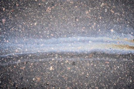 A vibrant oil slick stretches across the asphalt, reflecting various colors in the sunlight. This striking sight captures the interplay of light and pollution in the urban landscapeの写真素材