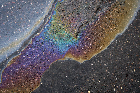 A puddle of gasoline or oil on a wet asphalt road highlighting environmental pollution.の写真素材