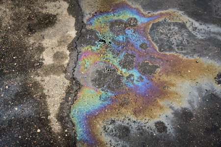 A shimmering gasoline spill creates a vibrant rainbow on asphalt, raising awareness of environmental pollutionの写真素材