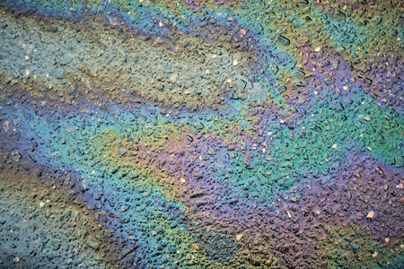 Vibrant swirls of color from an oil slick form intricate patterns on a wet pavement in an urban area, showcasing an unexpected beauty in everyday settingsの写真素材