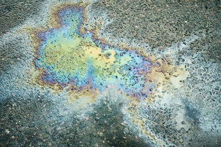 Oil Slick Reflecting Colorful Patterns on Asphalt During Daylight in an Urban Settingの写真素材