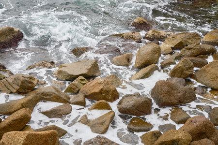 Rocky Shoreline With Crashing Waves Against Stones on a Cloudy Day at the Coastの写真素材