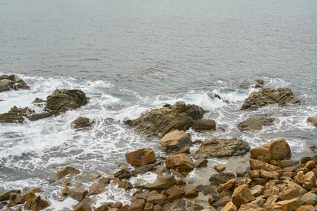Rocky Shoreline With Waves Crashing Against Boulders on a Calm Overcast Day at the Coastの写真素材