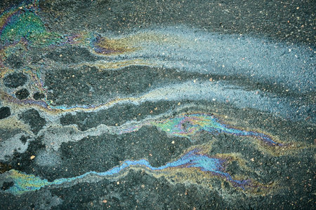 Colorful Oil Slick Contrasting With Dark Asphalt Captures a Unique Natural Pattern in a Urban Environmentの写真素材