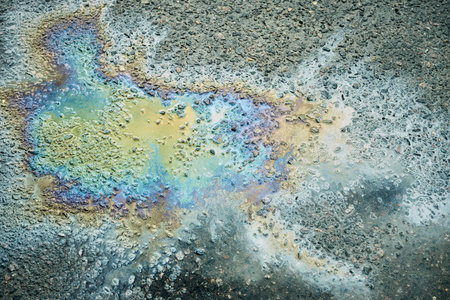 An oil slick on wet pavement refracts light, creating a vibrant array of colors and patterns,...