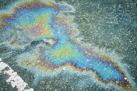 Colorful gasoline or oil spill creating a rainbow sheen on asphalt road, indicating pollution and environmental damage.の写真素材