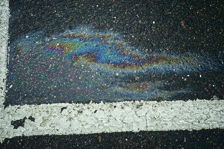 Oil slick spreads rainbow colors on wet dark asphalt next to a white line.の写真素材