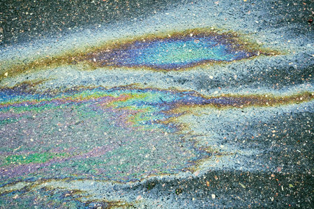 Oil spill on wet asphalt surface creating colorful iridescent rainbow patterns. Concept of...