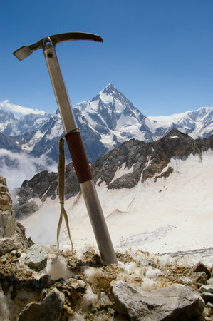 Ice ax stuck into the rock against the backdrop of the sunny mountain peak