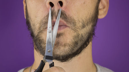 Handsome young guy trims his beard with scissors.