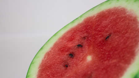 A slice of ripe watermelon rotates on a plate. Close up of watermelon pulp with seeds inside.の写真素材