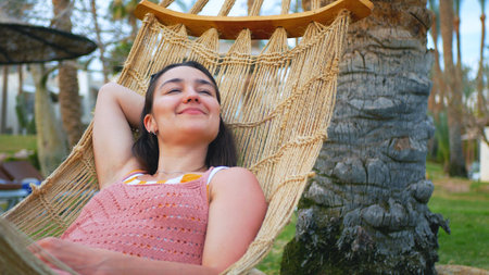 A young carefree girl lies in a hammock and enjoys her summer vacation.