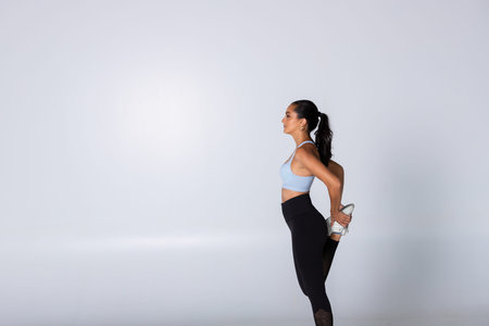 Fitness woman stretching her leg in sportswear on white background, female trainer isolated showing...