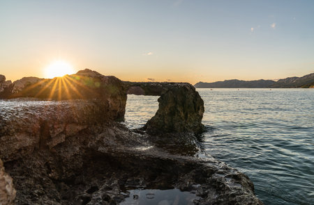 Seascape sunset. In the foreground is a huge stone with a large hole. Through the stone view of the sea. The rays of the setting sun.の写真素材