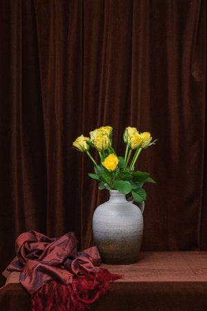 A beautiful bouquet of flowers of yellow roses in a gray vase on a background of dark brown fabric. Place for text, copy spaceの写真素材