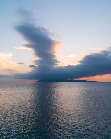 Sunset over sea. Dark water on the sea. An island on the horizon. Sunset clouds in sky. The beauty...