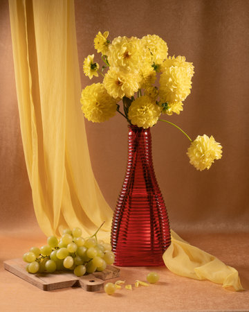Bouquet of yellow dahlias in a red vase and white grapes on the tableの写真素材