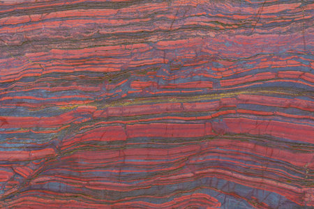 Faceted red stone with natural patterns and texture. Banded iron ore. Mineral structure, geological layers, natural background for design.の写真素材