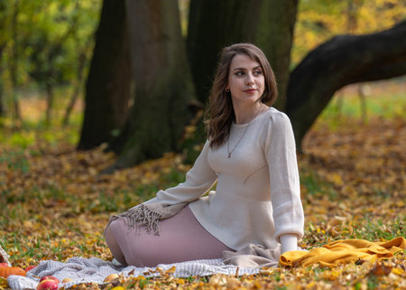 Portrait of a beautiful smiling girl with dark hair and big eyes. Autumn walk in the park. A girl sits next to a basket with apples, pumpkins, flowersの写真素材