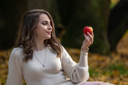 A beautiful girl with dark hair holds an apple in her hand and looks at the fruit. Choice,...